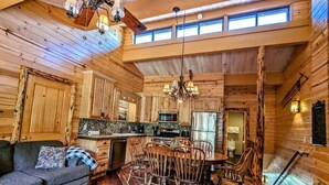 A log cabin interior with a dining area, kitchen, and a sofa.