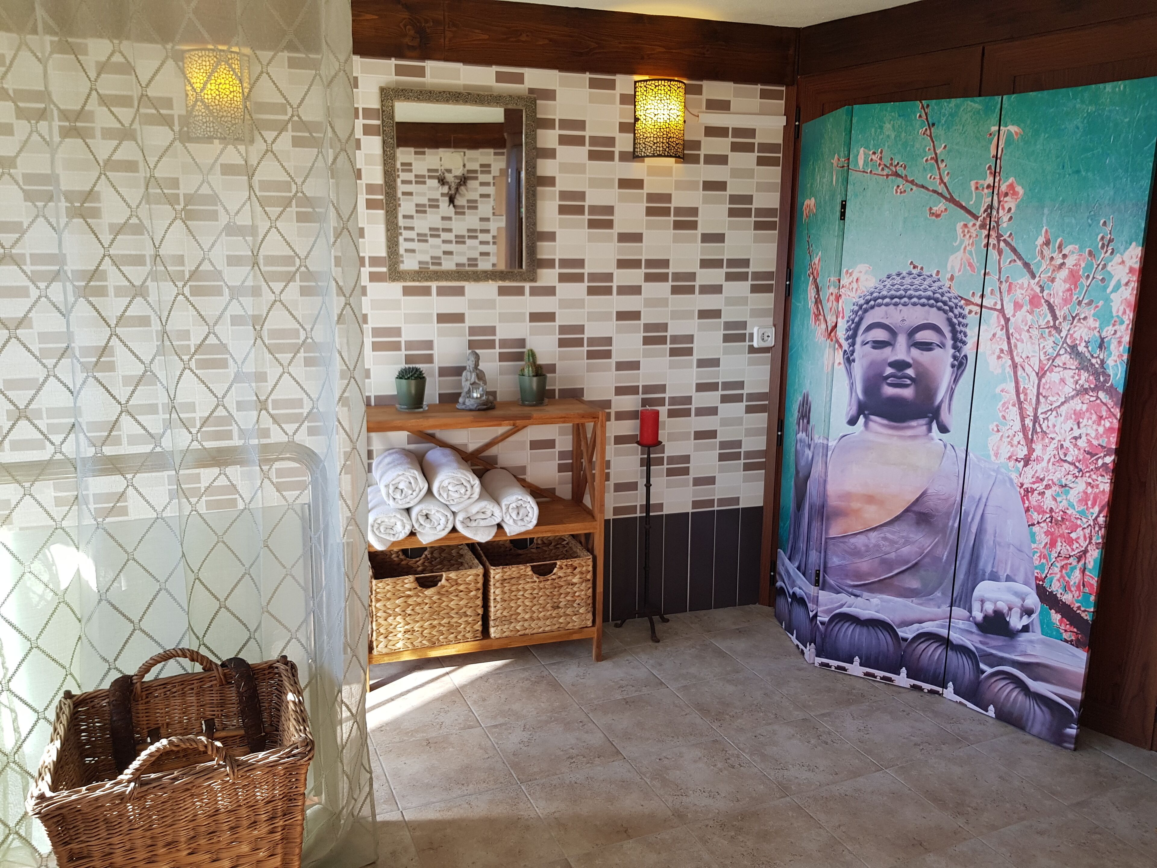 Une pièce avec un mur décoré de mosaïques, un tableau représentant Bouddha, une étagère avec des serviettes et des paniers en osier.