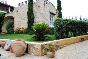 A stone building with a garden in front, including large pots and potted plants.