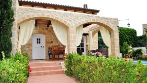 A stone building with a covered entrance, steps leading to a door, and a pool in the background.