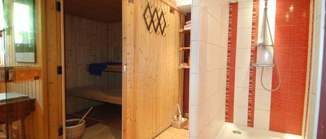 A sauna with a wooden door, a shower area with red tiles, and a small wooden shelf with towels.