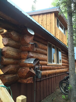 A log cabin with a metal roof, a window, and a bicycle parked outside. - Log Cabin W Bedroom Loft, Seperate private Bath House and Boat House (Sterling)