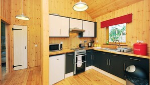 A compact kitchen with wooden walls, a microwave, stove, sink, and a red bread container. - Silver Birch Cabin - Charming Log Cabin with bags of character and hot tub. (Dalavich, Taynuilt)