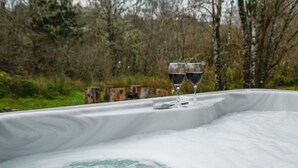 A hot tub with two glasses of red wine, surrounded by trees and greenery. - Silver Birch Cabin - Charming Log Cabin with bags of character and hot tub. (Dalavich, Taynuilt)