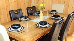 A wooden dining table set with black plates, clear glasses, and a vase with yellow flowers. - Silver Birch Cabin - Charming Log Cabin with bags of character and hot tub. (Dalavich, Taynuilt)