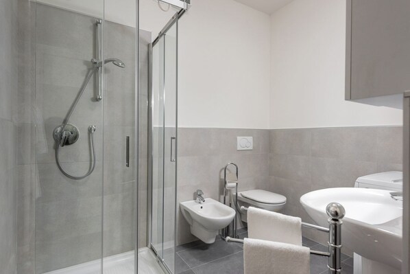 Un baño moderno con ducha de vidrio, un bidé, un inodoro y un lavamanos.