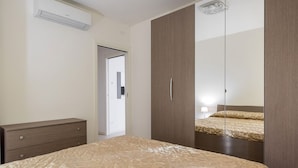A bedroom with a bed, a wardrobe, a dresser, and an air conditioning unit.