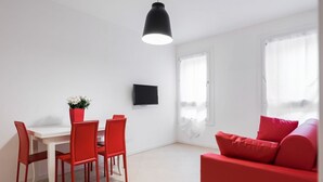 A modern living room with a red sofa, a dining table with red chairs, and a TV mounted on the wall.
