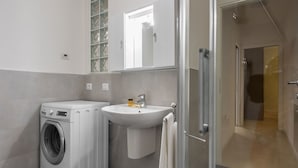 A modern bathroom with a washing machine, sink, and glass shower enclosure.