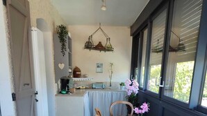A dining area with a table set for four, a kitchen in the background, and a window with blinds. - house with pool in beausset (Le Beausset)