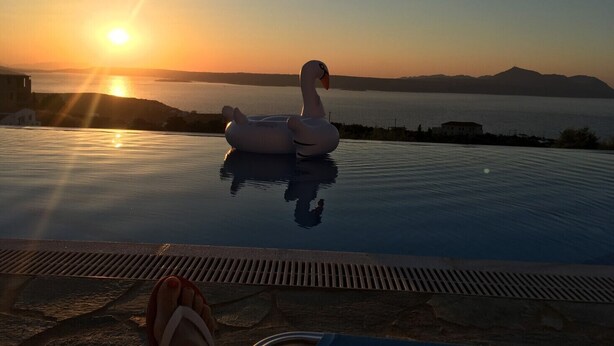 A swan-shaped float on a pool at sunset with a view of the sea and distant hills.