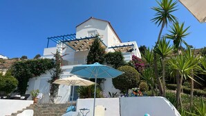 A white building with a blue roof, a covered outdoor seating area, and a staircase leading to the entrance.