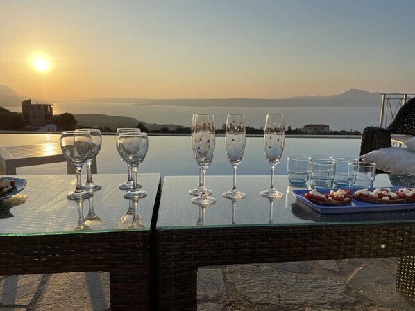 A table set with wine glasses and a plate of appetizers, overlooking a scenic view with mountains and a body of water during sunset. - Big infinity private pool (10mtx4mt)★Sea view★Big sea view terrace 100m2★ (Kokkino Chorio)