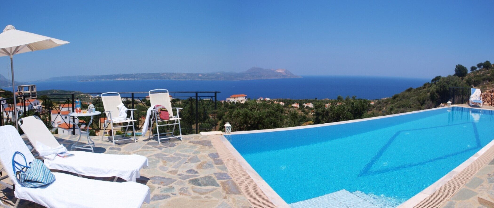 A swimming pool with lounge chairs and an umbrella, overlooking a coastal landscape.