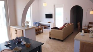 A modern living room with a sofa, a dining table with chairs, and a kitchen area with a TV.