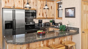 Una cocina moderna con armarios de madera, electrodomésticos de acero inoxidable y encimeras de granito, además de taburetes de bar.
