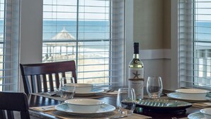 A dining table set for four with a bottle of wine, glasses, and plates. - SC302 C-View by First Flight Rentals (Kill Devil Hills)