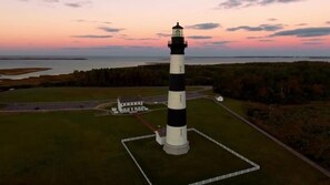 Un faro con torre a rayas blancas y negras, rodeado por una cerca y un pequeño edificio cercano.