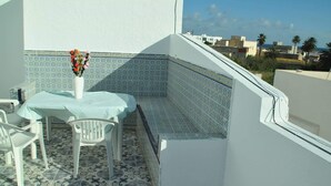 A small outdoor balcony with a table and chairs, patterned tiles, and a view of buildings and palm trees. - City Apartment on the port of Mahdia Free Wifi (Mahdia)