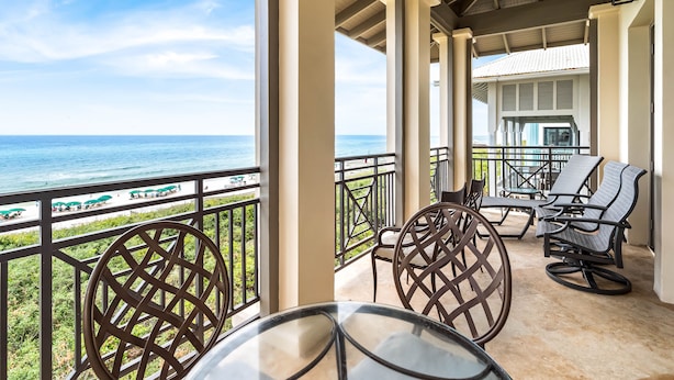 A covered balcony with a view of the ocean, featuring a glass table and wicker chairs.