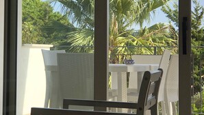 A balcony with a white chair, a small table, and a view of palm trees and greenery.