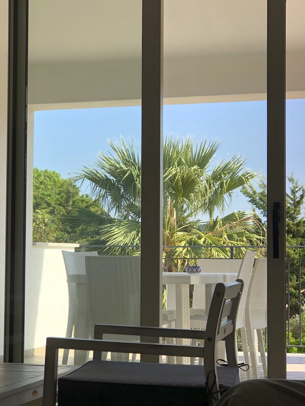 A balcony with a white chair, a small table, and a view of palm trees and greenery.