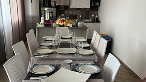 A dining area with a table set for six, surrounded by white chairs, in a modern kitchen with cabinets and a tiled backsplash.