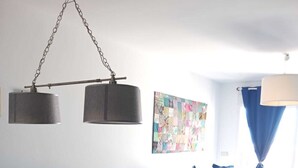 Ein Essbereich mit einem Holztisch, stuhlförmigen Sitzgelegenheiten mit Blumenmuster, einer hängenden Leuchte und einer farbenfrohen Wanddecke.