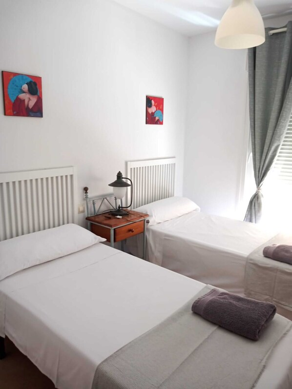 Une chambre d’hôtel avec deux lits simples, une table de chevet avec une lampe, un radiateur et deux tableaux accrochés au mur.