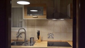 Eine Küche mit einer Edelstahlspüle, einem eingebauten Ofen und einer Mikrowelle. Ein Fenster mit Jalousien, eine Pendelleuchte und ein Messerblock auf der Arbeitsplatte sind vorhanden.