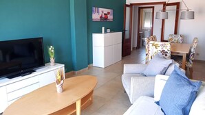 Ein Wohnzimmer mit Fernseher, einer Couch, einem Couchtisch und einem Essbereich mit Stühlen und einem Tisch.