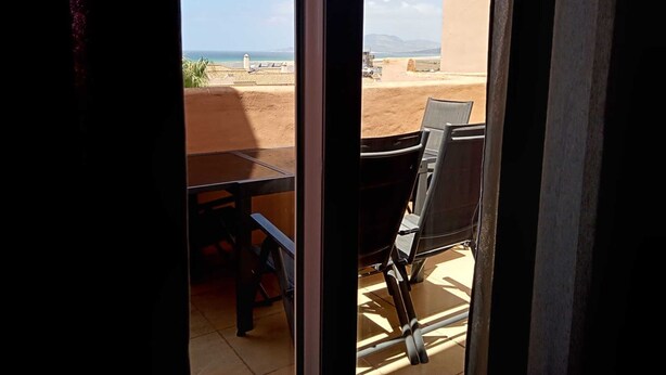 Ein Balkon mit Tisch und Stühlen, mit Blick auf Strand und Berge.