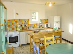 Une cuisine compacte équipée d’un four à micro-ondes, d’une cuisinière et d’un réfrigérateur. Elle comprend une table et des chaises en bois, une fenêtre et un revêtement mural coloré en carreaux.