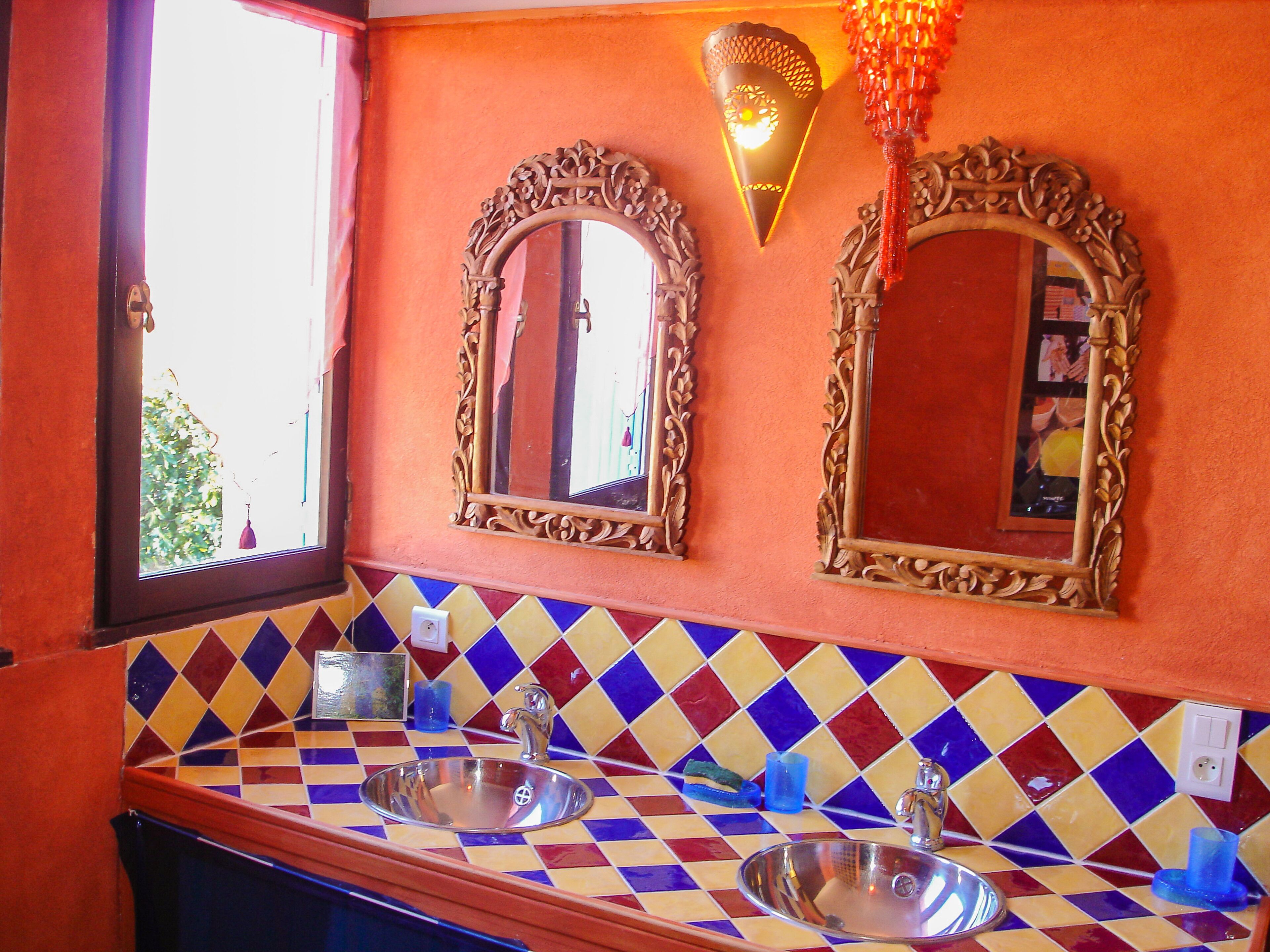 Une salle de bain avec deux lavabos, un miroir et un luminaire décoratif fixé au mur.