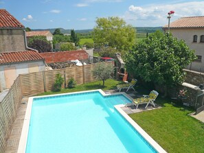 Ein Pool mit Holzterrasse und Liegestühlen, umgeben von einer Steinmauer und viel Grün.