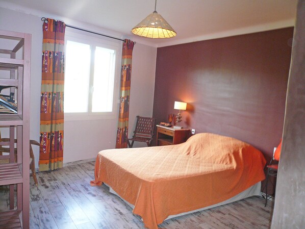 A bedroom with a bed, a chair, a desk, a lamp, a shelf, and a window with curtains.