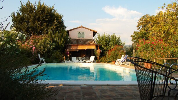 A swimming pool with lounge chairs, surrounded by lush greenery and a house with a tiled roof. - B&B with pool, only one step away from Assisi (Bastia Umbra/Assisi)