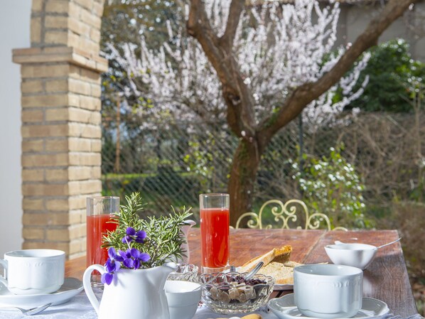 Ein Frühstückstisch mit zwei Gläsern rotem Getränk, einer Karaffe, einer Obstschale und einer weißen Teekanne.