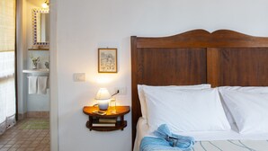 A bedroom with a wooden headboard, a bedside table with a lamp, a framed picture on the wall, and a bathroom visible through an open door. - B&B with pool, only one step away from Assisi (Bastia Umbra/Assisi)