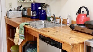 A kitchen with wooden cabinets, a sink, a dishwasher, and a kettle. - Private Lake at Rippling Waters One Room Cabin (Delhi)