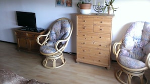 A living room with two wicker chairs, a wooden cabinet, a television, and a decorative poster on the wall. - Curr. M.Flair, quiet location, grGarten, fenced.2km, directly to the forest / meadow, gr. Lake (Blankenheim-Reetz)