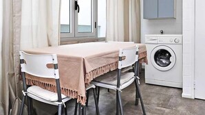 A small, clean room with a table and chairs, a washing machine, and a window with curtains. - Sweet Garden Cascais - Checkinhome (Cascais)