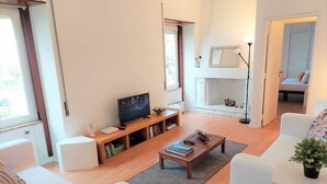 A modern living room with a flat-screen TV, a bookshelf, and a fireplace. - Sweet Garden Cascais - Checkinhome (Cascais)
