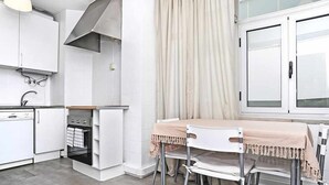 A modern kitchen with white cabinets, a built-in oven, and a dining area with a table and chairs. - Sweet Garden Cascais - Checkinhome (Cascais)