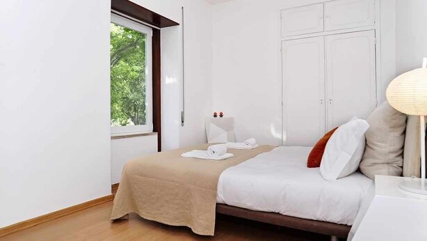 A bedroom with a bed, a bedside table, a lamp, and a wardrobe. - Sweet Garden Cascais - Checkinhome (Cascais)