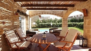 Eine Terrasse im Freien mit einer Steinwand, einem runden Holztisch und vier gepolsterten Stühlen.