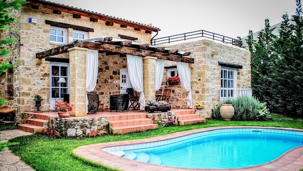 Ein Steinhaus mit Pool, Treppen zu einer überdachten Terrasse und Gartenmöbeln.