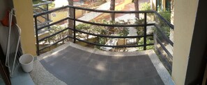 Un balcon avec une rambarde en métal, un seau blanc et une vue sur un terrain de jeux et des bâtiments en arrière-plan.
