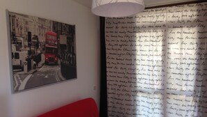 A room with a red sofa, a black and white street scene painting, and a curtain with handwritten text.