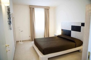 A bedroom with a bed, a nightstand, a lamp, and a window with curtains. - Swimming pool with sea view , for families,  historic center  700 m, beach  8'  (Ostuni)